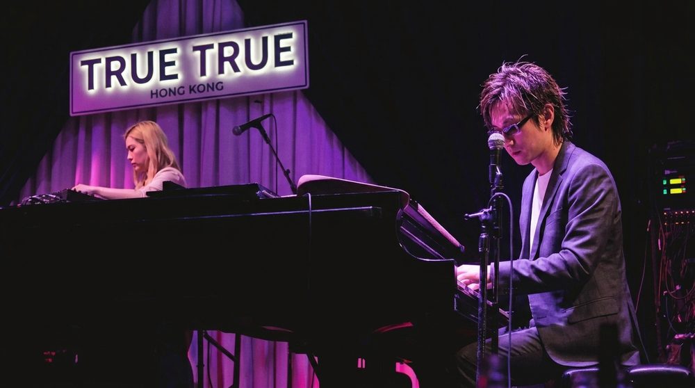 陳子詠喺 True True 舞台彈鋼琴唱歌，紫色燈光；另一位樂手喺旁邊彈另一部鋼琴